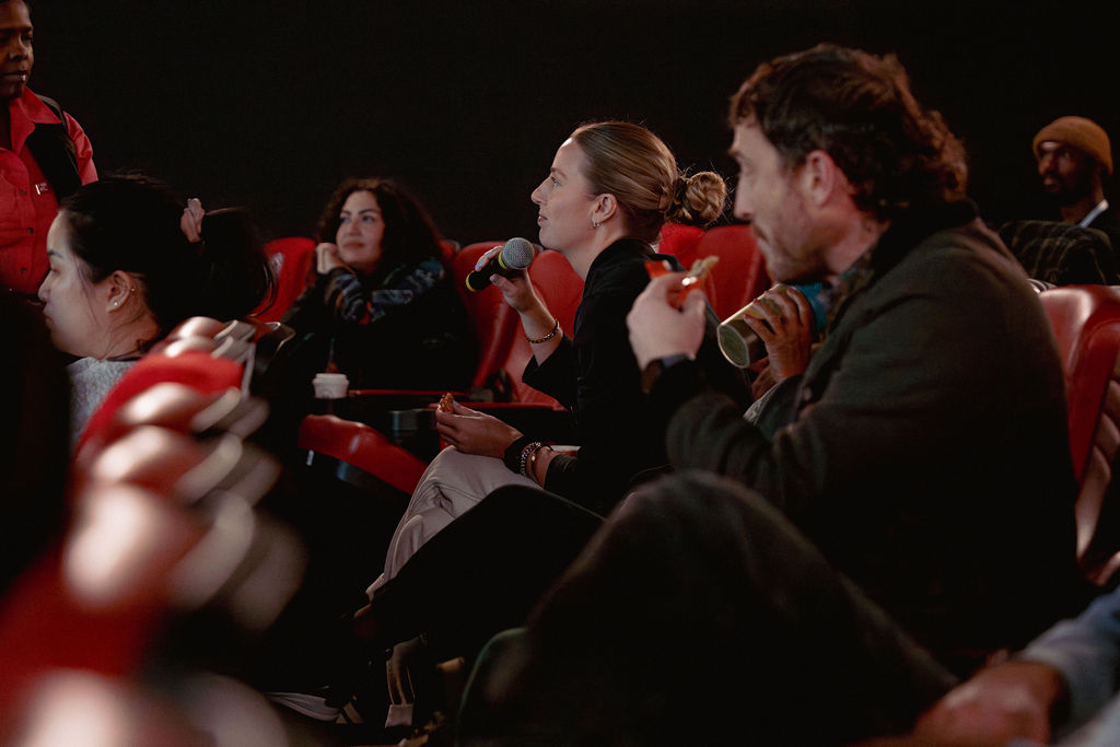 Members of a darkly lit theater audience asking a question to someone on stage