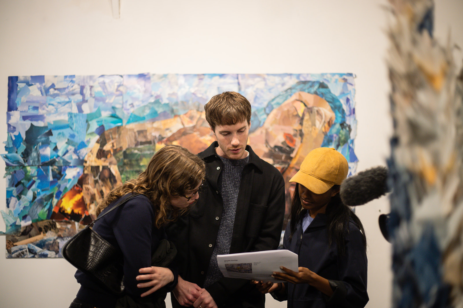 3 people gathered in front of a brightly painted image and discussing a document they are holding
